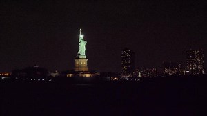 Illuminated Statue of Liberty at Night and Buildings of New York City. View from the Water. Orbiting