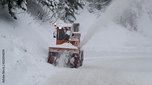 Footage of a snow removal machine removing snow from a road in the mountains