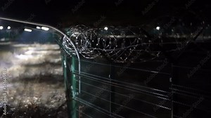 Perimeter security fencing system. Welded wire mesh fence line with lighting and razor wire at night.