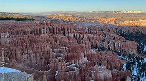 Beautiful panning shot of Bryce Canyon's Amphitheater at sunset with snow on the ground. The golden light illuminates the red rock hoodoo formations - Utah, USA