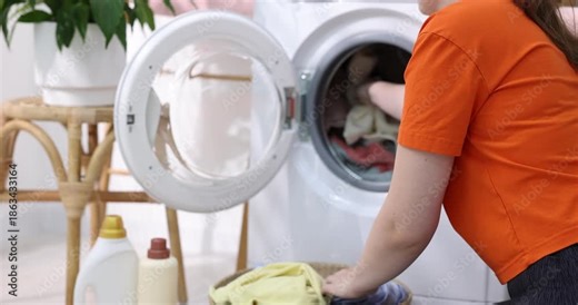 Woman taking laundry from basket and putting into washing machine indoors, closeup