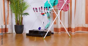 Round robot vacuum cleaner rides on floor of cozy room, sucks up garbage, thing that lying on floor. New technology cleaning assistants. Automation replacing people with robots. Chores freeing up time