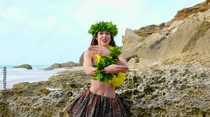 Pretty and energetic woman performing hawaiian dancing on the beach with blanks. The perfect landscape.