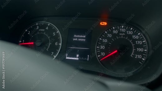 Car dashboard indicating parking sensor warning with stationary needles at idle, Dashboard speedometer alongside center display presenting parking sensor message with amber warning lamp idle