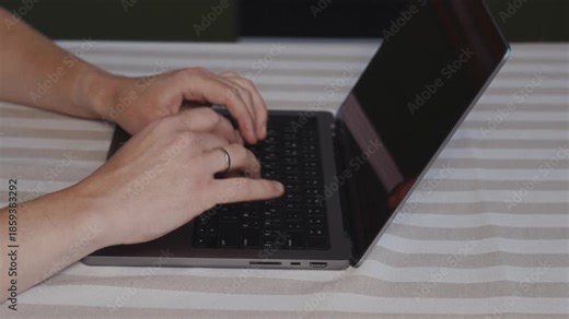 Wider close up of male hands typing on a laptop keyboard placed on a table. Natural arm position, smooth finger movement and calm everyday computer work indoors. High quality 4k footage