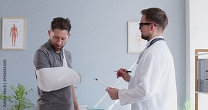Doctor traumatologist giving recommendations to man wearing sling on broken arm, rehabilitation after injury. Male patient with hand protective bandage, trauma rehabilitation, healthcare insurance