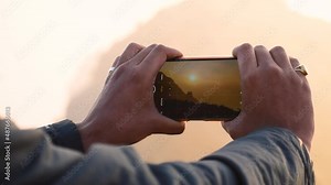 Close up of Male hands using smartphone and clicking photos of Girnar mountain. Photographer Creating multimedia content of mountains during sunrise, man clicking pictures during trekking adventure.