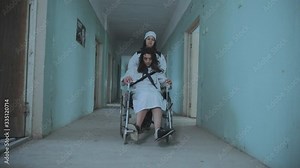 Female Nurse Pushing Patient In The Wheelchair Through The Hospital Corridor