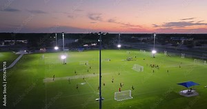Illuminated public sports arena in North Port, Florida with people playing soccer game on grass football stadium at sunset. Outdoor activities concept