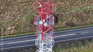Mountain road adjacent to a metal cell tower, painted white and red, amidst a picturesque autumn setting.