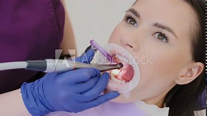Proficient female dentist in gloves removes damaged part of tooth with dental drill. Cavities treatment process in private dental clinic