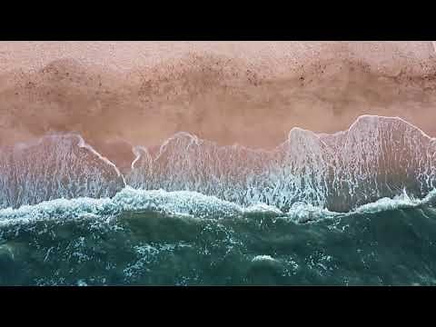 Sandy beach and blue sea, foaming waves on the coast. Aerial view from above. Drone footage