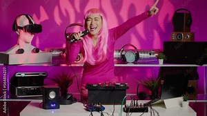 Cheerful performer having fun mixing techno sounds in night club, playing music using professional turntables. Asian artist standing at dj table dancing while celebrating techno album with fans