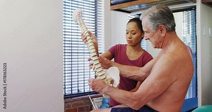 Physiotherapist explaining the spine model to senior patient