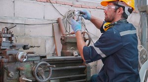 Young caucasian engineer man operating lathe machine for preparing production at factory industrial, technician or labor maintenance machinery at workplace, metalworker working, industry concept.