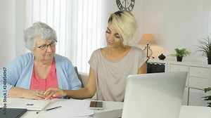 young woman helping an old senior woman doing paperwork and administrative procedures with laptop computer at home