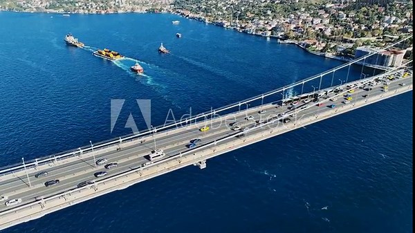 Aerial view of the Istanbul Bosphorus Bridge with drone on a cloudy day. Tanker ship passing under the FSM Bridge with a heavy car traffic on the bridge.