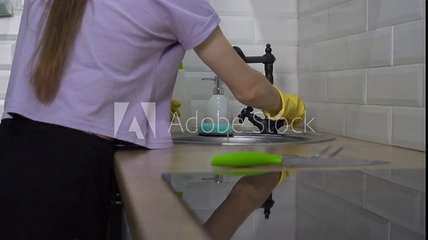 Woman putting on yellow rubber protective gloves to wash dishes in the kitchen and turning on the faucet. Concept of housekeeping, housework