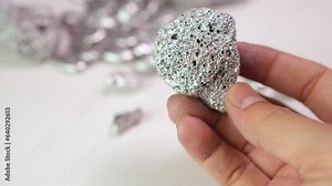 Man's hand holding a lump of silver or platinum or a rare earth mineral on white background