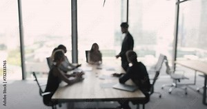 Business team meeting at large table in office space with large window, talking, brainstorming on ideas, listening to standing speaker. Negotiations of partners, teamwork blurred background