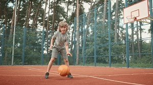 Happy positive cute teen boy bouncing ball practicing basketball moves outdoor on court. Caucasian little cheerful child playing basketball. Dribble moves. Fun. Leisure activity. Childhood concept