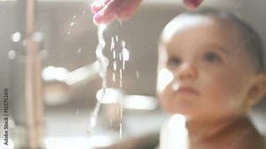 Mother Hand Checks Water Temp with Child. a close up of a woman's hand testing and feeling the temperature of the water while a child looks on in the background. Slow motion