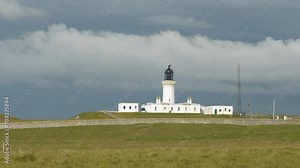 TIME LAPSE: White lighthouse basks in the sun as dark clouds roll above it. Constantly changing weather on the north coastline of Scotland. Beautiful view of the still operating Noss Head Lighthouse.