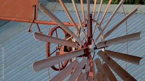 Close Up view of rust coloured spinning windmill with tin roofs in the background. locked off
