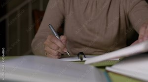 Woman doing her assignment by referring to books and writing on notepad.