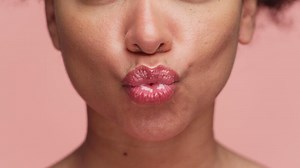 Close-up of woman puckering lips for a kiss on pink