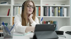 Young blonde woman student using touchpad writing on notebook at university classroom