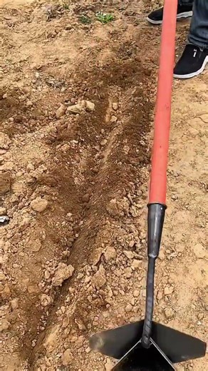 Person digging narrow trench with triangular soil tool