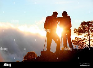 Hiking adventure healthy outdoors people standing talking. Couple enjoying sunset view above the clouds on trek. Video of young woman and man in nature wearing hiking backpacks and sticks Stock Photo - Alamy