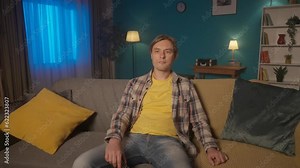 Sleepy tired man watching TV while sitting on the couch late at night. A man falls asleep with a remote control to a boring, uninteresting movie. Sleeping man close up. HDR BT2020 HLG Material.