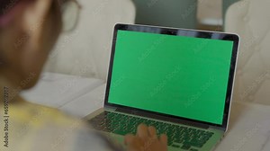 Over the shoulder shot of woman, using finger with keyboard for typing touch. computer laptop with blank green screen chroma key in cafe.