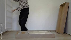 The old man opens a large parcel. Grandfather opens a cardboard box. The baby bed is packed in a large box. The man takes a wooden piece of the bed out of the box.