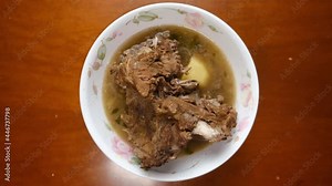 Low exposure and noise effect added footage of rotating homemade "sup tulang" on the table. Is an aromatic beef soup flavored with spices like coriander, cinnamon, chili, onions and aniseed.