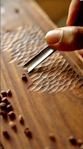 Hand carving textured, wave-like or scaled patterns into dark wood using a sharp gouge