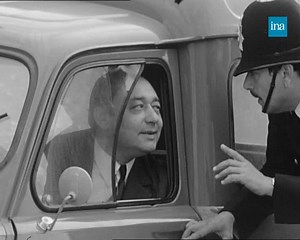 🇬🇧 ROULEZ À GAUCHE. Les équipes de la «Caméra invisible» ont transformé un petit village d'Île-de-France en territoire britannique : panneaux de signalisation, figurants et publicités anglaises forment le décor. L'acteur Jacques Legras, en bobby, arrête les conducteurs et leur demande, avec un fort accent, de rouler à gauche... Mais par moments, ce dernier est trahi par sa notoriété ! | INA