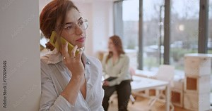 Focused businesswoman multitasking in a vibrant office environment, checking her watch while having business call.