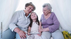 Old great-grandmother and grandma nanny kissing and hugging cute small preschool little girl with digital tablet. Three generation family at home, Female family enjoy, respect and warm relation