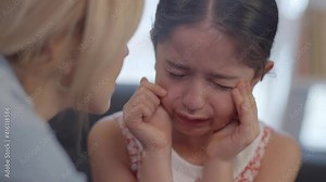 Pretty little girl cries while sitting on the sofa.Loving mother trying to calm her sad crying little daughter. Portrait of really crying little girl. Slow motion and close up video.
