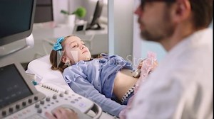 Cute little girl having ultrasound procedure of internal organs with sonographer at medical clinic. Pediatric abdominal ultrasound