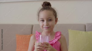 Cute little girl drinking a glass of milk in the kitchen at home. Slow motion little girl drinking water. Close-up. The child drinks milk from a glass.