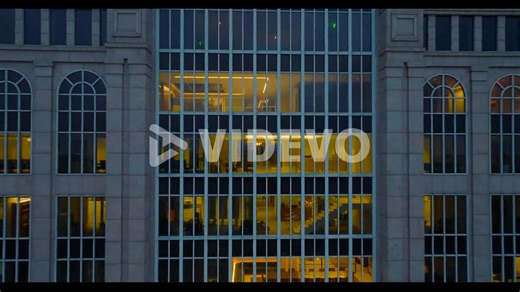 Pull back shot of illuminated interior of high rise commercial building at dusk