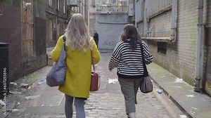 Two females walk along a alleyway followed closely by a suspicious man