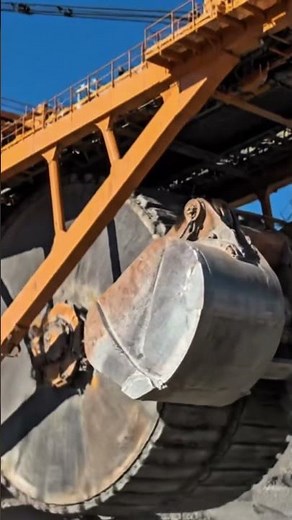 A massive bucket-wheel excavator working in a mining site under a clear blue sky