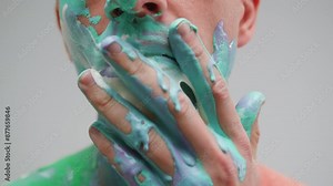 Man is drawing colourful paints on his face by hand close-up. Body art therapy with many various of paints. Painting on human body.
