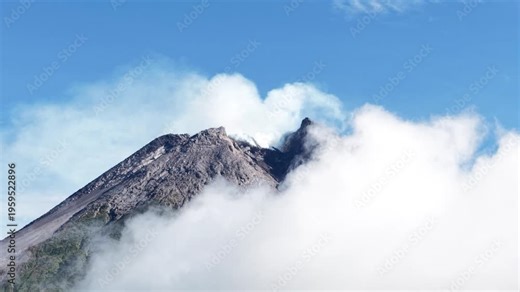4K aerial footage shows the peak of Mount Merapi in Yogyakarta covered in thick clouds, with clear blue skies.