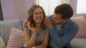 Couple embracing on a couch where a man comforts a crying woman in a cozy living room with soft light and neutral decor, suggesting a quiet moment of relationship support and affection